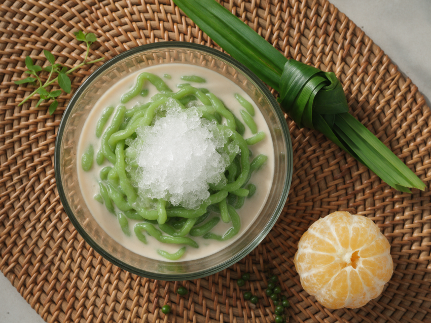 Overhead view of green pandan lod chong noodles in coconut milk with crushed ice in a glass bowl on a rattan mat