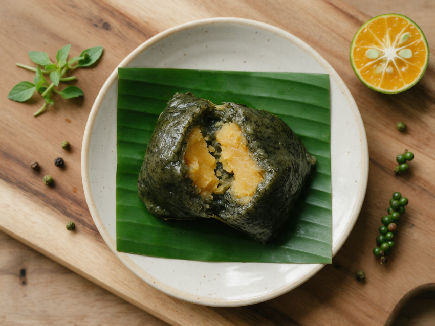 Sliced bánh ít lá gai on banana leaf showing dark rice dough wrapped around golden mung bean filling