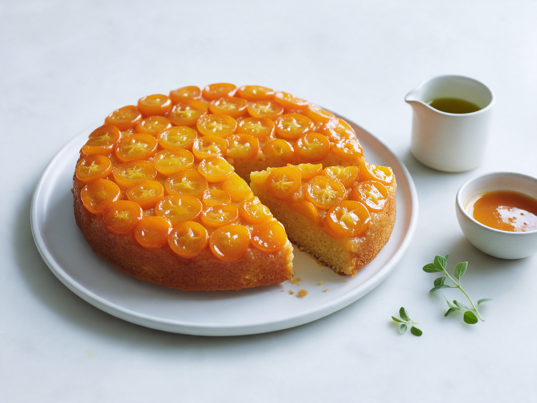 Overhead view of upside-down kumquat cake on a white plate, glossy orange slices over golden crumb